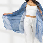 Close Up of A woman modeling a Chambray striped fringed Kaftan or wrap over a white crop top and white Pants, standing against a white studio wall.