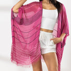 Close Up of A woman modeling a bright pink and magenta striped fringed Kaftan or wrap over a white crop top and white shorts, standing against a white studio wall.