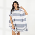 A woman wearing a classic stripe hooded beach poncho with fringed tassels along the hem, photographed against a clean white studio background.