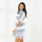 A woman wearing a classic stripe hooded beach poncho with fringed tassels along the hem, photographed against a clean white studio background.