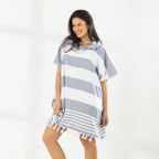A woman wearing a classic stripe hooded beach poncho with fringed tassels along the hem, photographed against a clean white studio background.