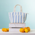 A cooler lunch bag, displayed on a stack of two white wooden crates with oranges and lemons on a light-colored table against a light blue background.