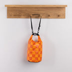 Seaside Supplies Waterproof Beach Bag 8L Check featuring a vibrant orange and yellow checkerboard design with a roll-top closure, black buckle fastening and adjustable shoulder strap.