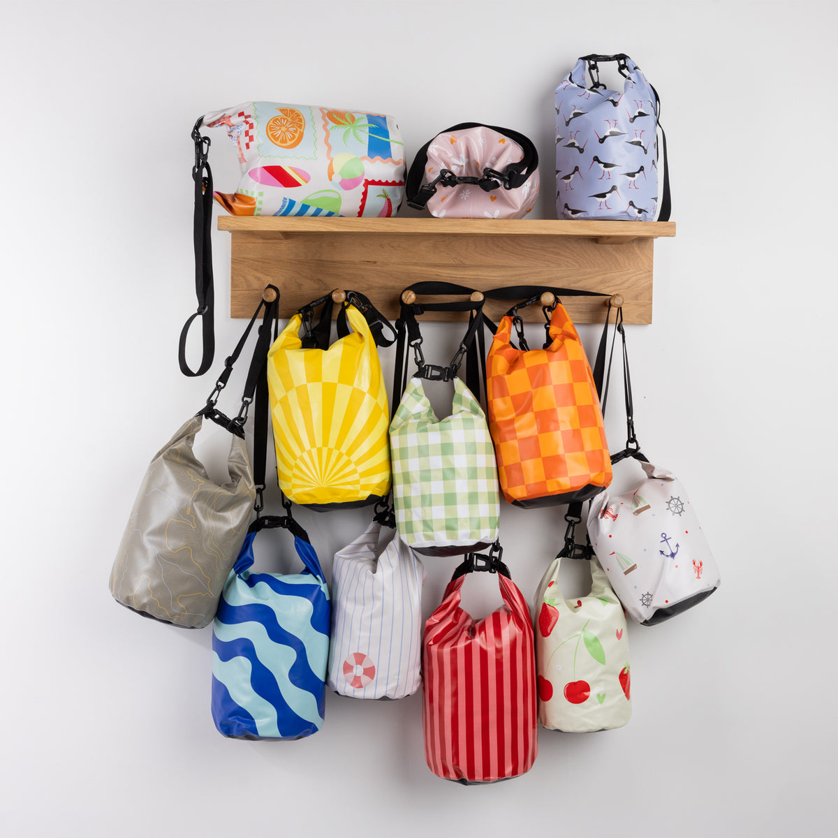 Seaside Supplies Waterproof Beach Bags Range featuring assorted 8L and 5.8L waterproof bags in colourful prints, displayed on a wooden wall shelf with hanging straps.
