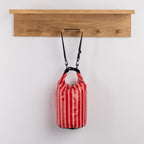 Seaside Supplies Waterproof Beach Bag 8L Red Stripe featuring bold red and pink vertical stripes with a roll-top closure, black buckle fastening and adjustable shoulder strap.
