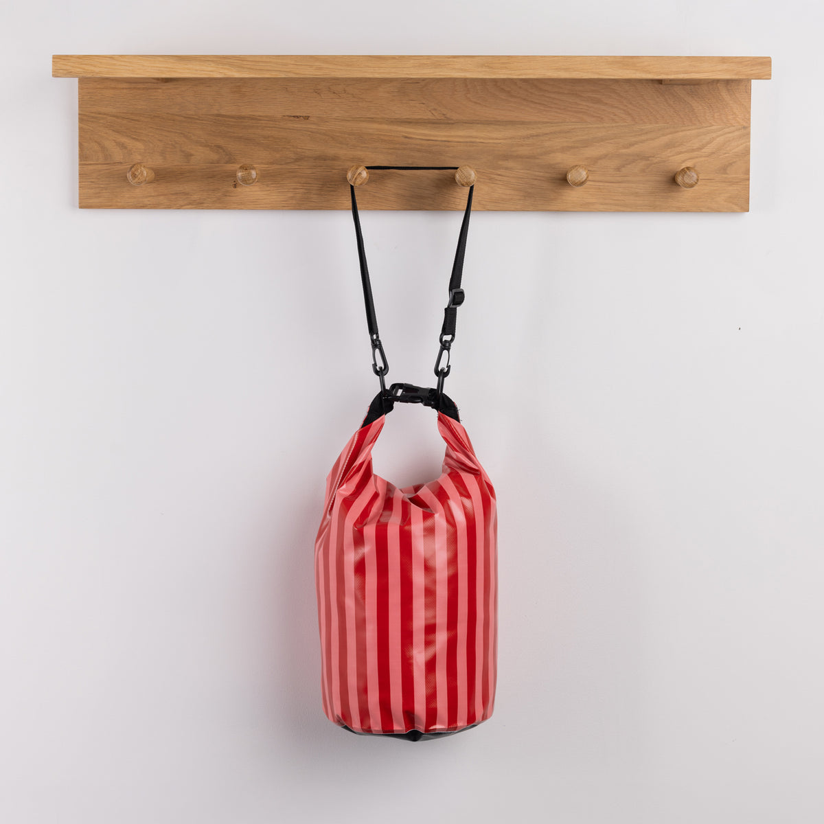Seaside Supplies Waterproof Beach Bag 8L Red Stripe featuring bold red and pink vertical stripes with a roll-top closure, black buckle fastening and adjustable shoulder strap.