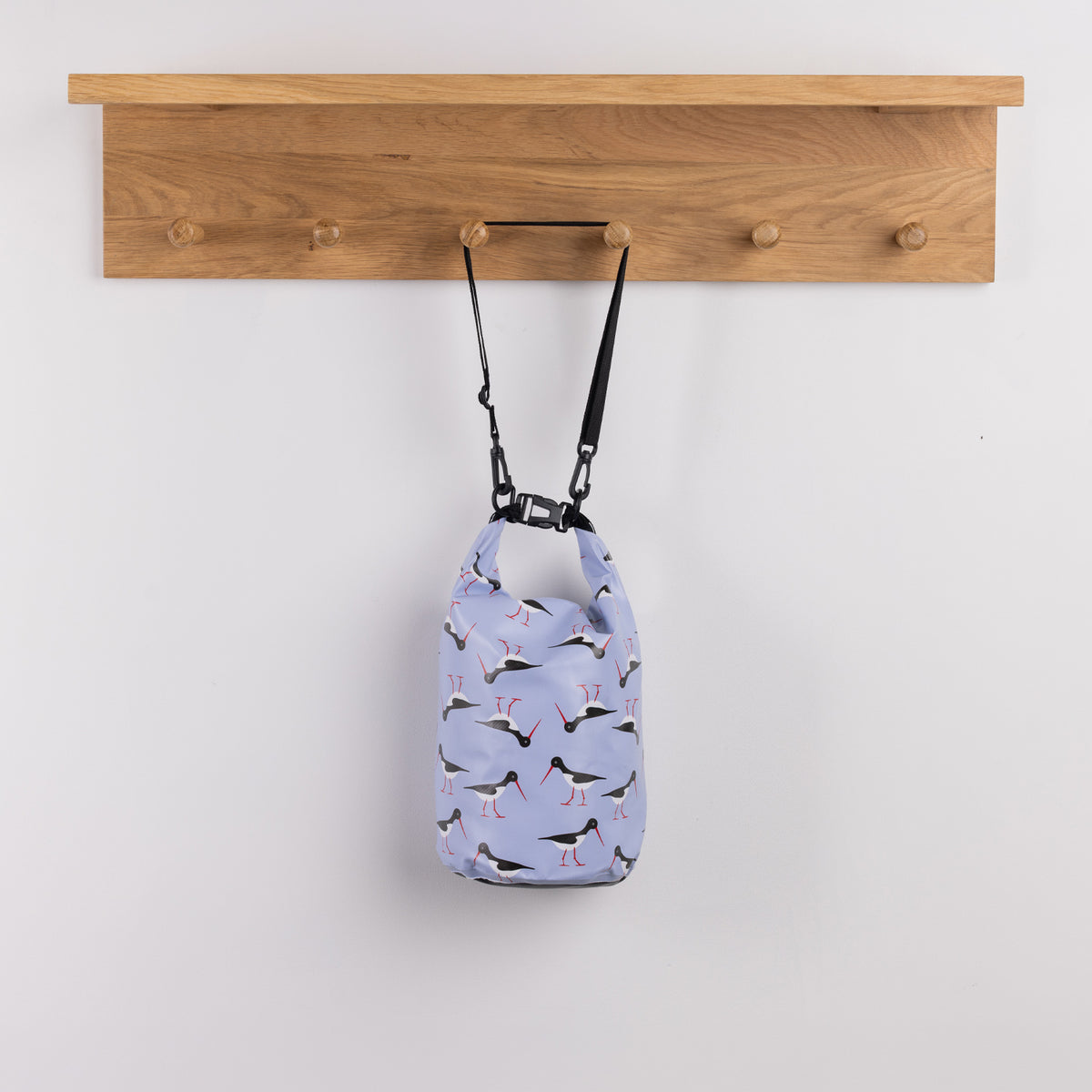 Seaside Supplies Waterproof Beach Bag 5.8L Oyster Catchers featuring a light blue background with repeating black and white oystercatcher birds, red legs and long red beaks.