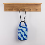 Seaside Supplies Waterproof Beach Bag 8L Wave Blue featuring a bold blue and light blue wavy design with a roll-top buckle closure and adjustable black shoulder strap.