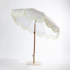 Seaside Supplies floral outdoor umbrella shown tilted, featuring a cream floral-patterned canopy with scalloped edges and fringe trim.