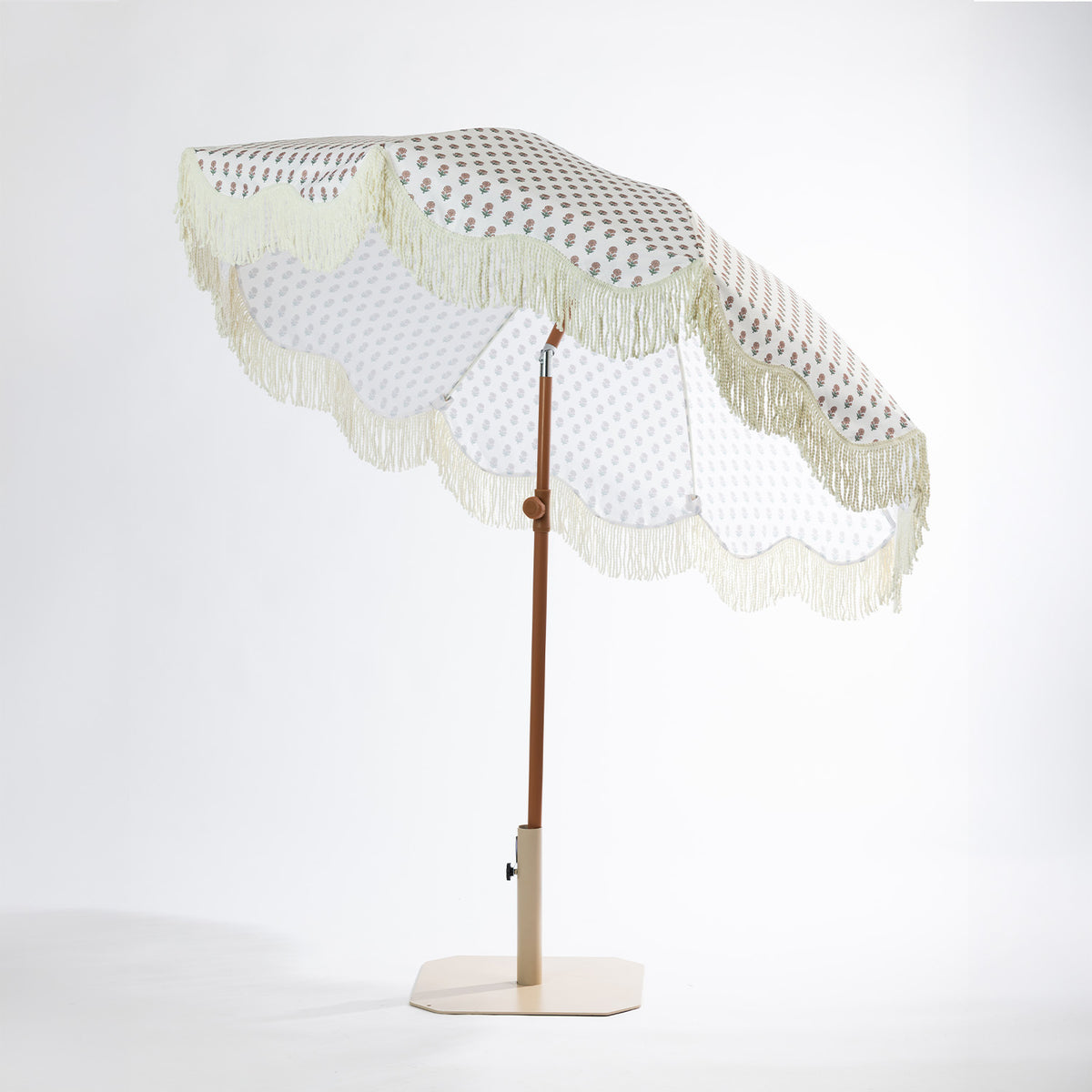 Seaside Supplies floral outdoor umbrella shown tilted, featuring a cream floral-patterned canopy with scalloped edges and fringe trim.
