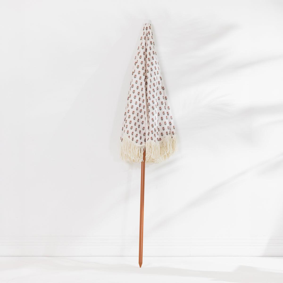 Seaside Supplies Floral Beach Umbrella featuring a cream canopy with a delicate floral print, cream fringed edges and a brown pole, displayed folded against a white background.