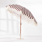 Brown and white striped umbrella with cream fringe trim, shown tilted on a matching cream base.