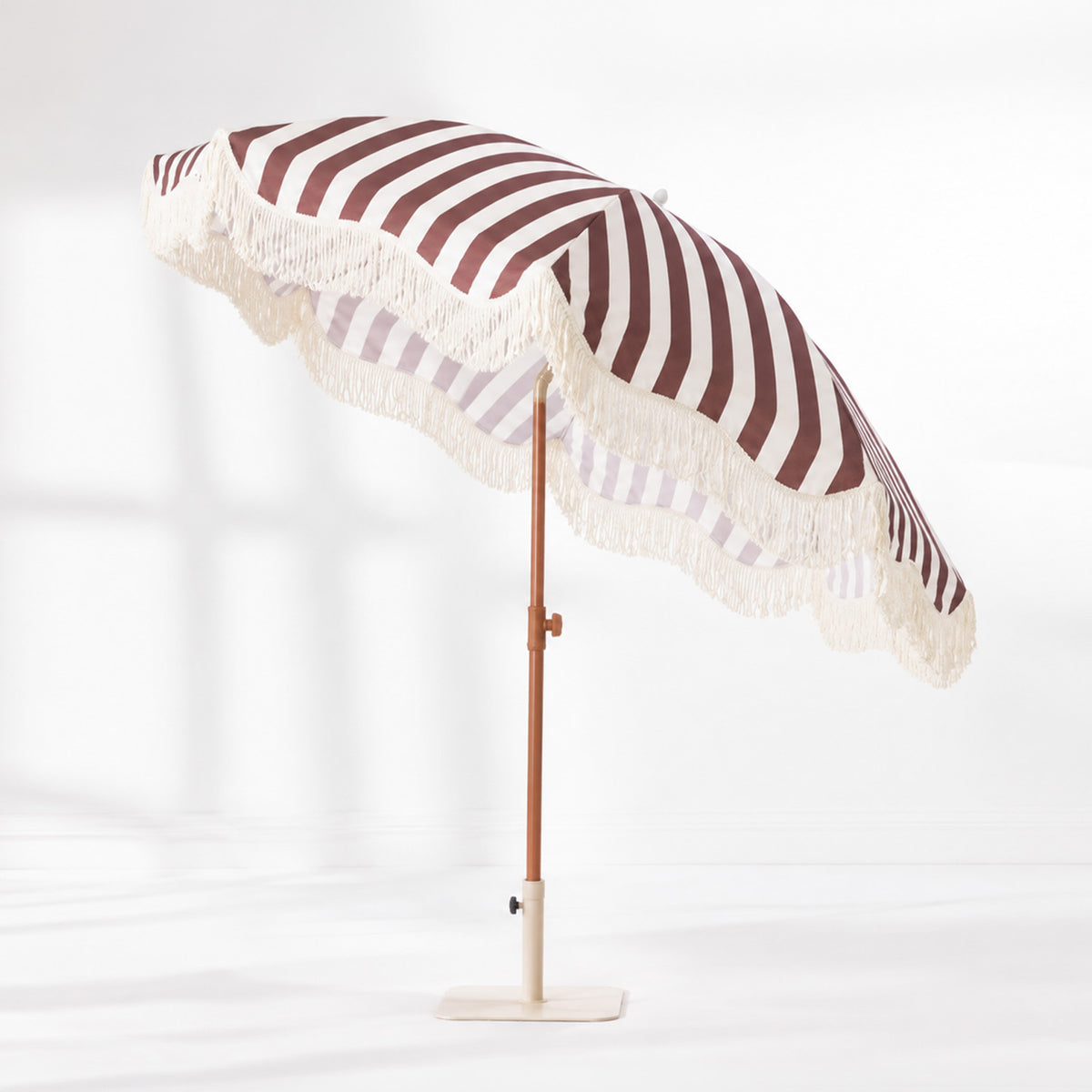Brown and white striped umbrella with cream fringe trim, shown tilted on a matching cream base.
