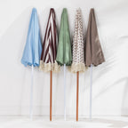 Five folded beach umbrellas in light blue, brown and cream stripe, sage green, floral print and taupe, displayed upright against a white background.
