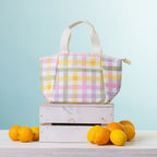 A cooler lunch bag, displayed on a stack of two white wooden crates with oranges and lemons on a light-colored table against a light blue background.