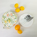 A round fabric picnic bag set with a white plates of silver cutlery styled with citrus fruits on a light wood background.