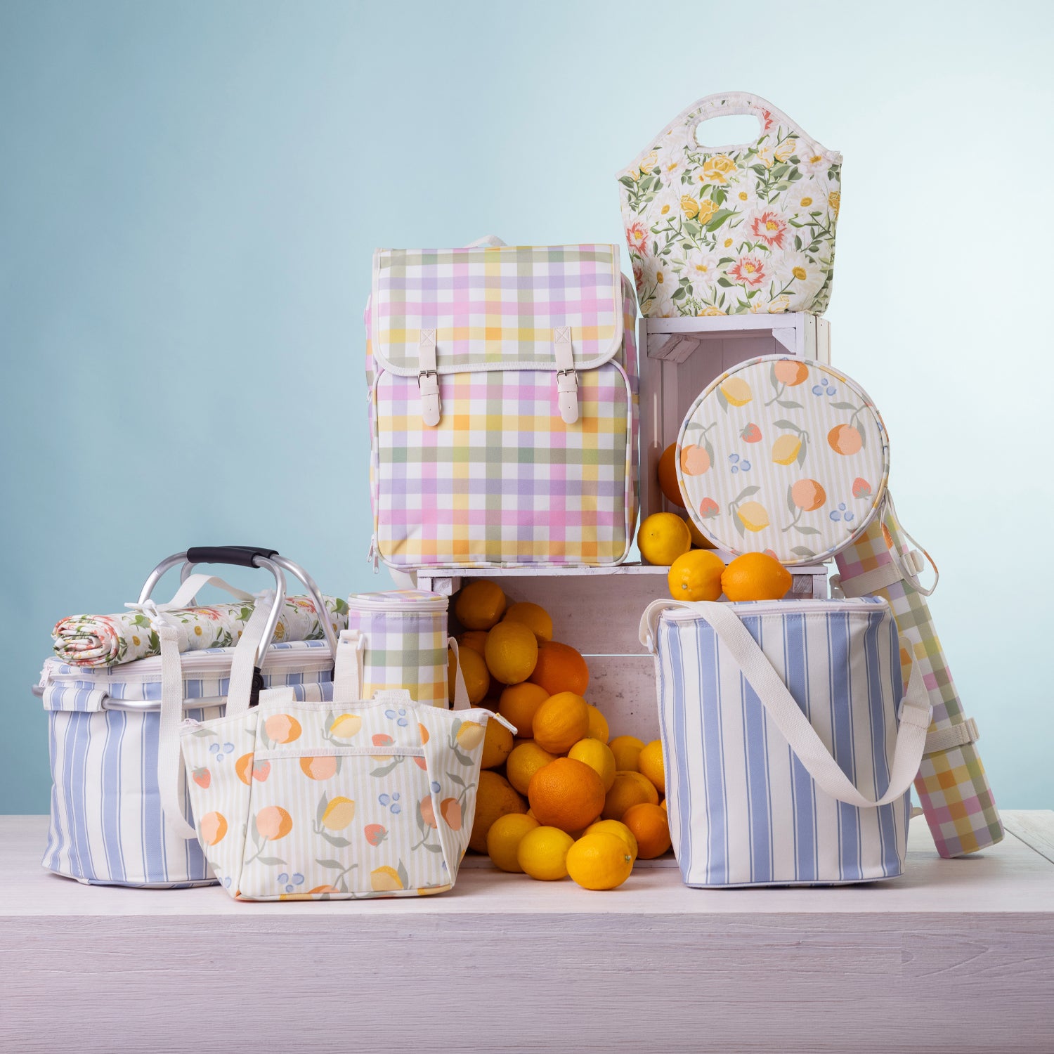 A coordinated range of picnic bags arranged on a white table with oranges in front against a soft light blue background.