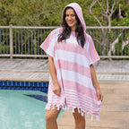 A woman wearing a striped hooded beach poncho with tassels, standing next to a swimming pool.