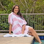 A woman wearing a striped hooded beach poncho with tassels, standing next to a swimming pool.
