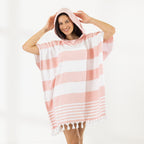 A woman wearing a classic stripe hooded beach poncho with fringed tassels along the hem, photographed against a clean white studio background.