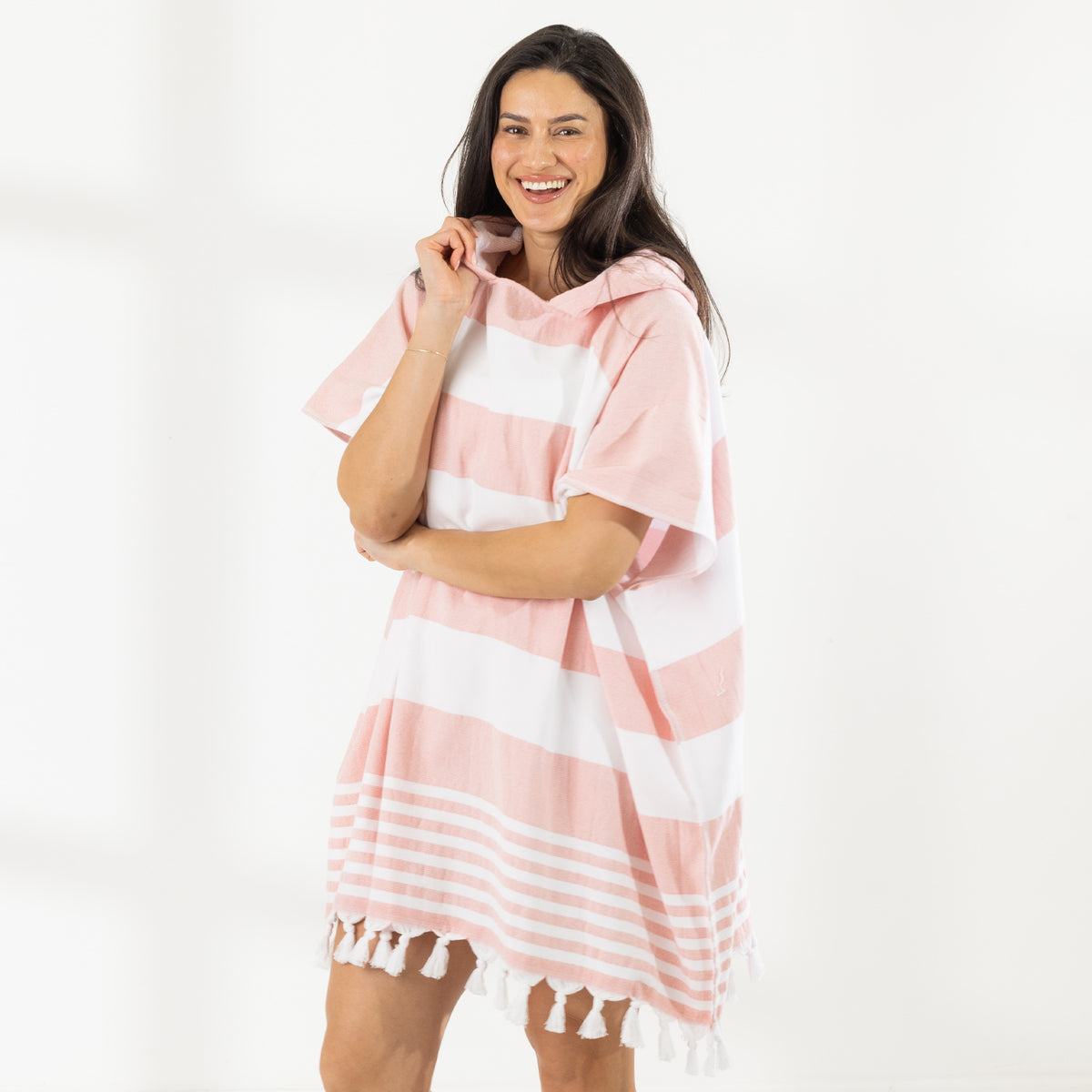 A woman wearing a classic stripe hooded beach poncho with fringed tassels along the hem, photographed against a clean white studio background.