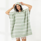 A woman wearing a classic stripe hooded beach poncho with fringed tassels along the hem, photographed against a clean white studio background.