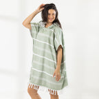 A woman wearing a classic stripe hooded beach poncho with fringed tassels along the hem, photographed against a clean white studio background.