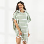 A woman wearing a classic stripe hooded beach poncho with fringed tassels along the hem, photographed against a clean white studio background.