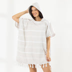 A woman wearing a classic stripe hooded beach poncho with fringed tassels along the hem, photographed against a clean white studio background.