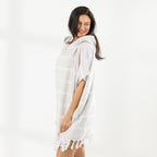 A woman wearing a classic stripe hooded beach poncho with fringed tassels along the hem, photographed against a clean white studio background.