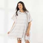 A woman wearing a classic stripe hooded beach poncho with fringed tassels along the hem, photographed against a clean white studio background.