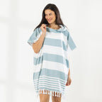 A woman wearing a classic stripe hooded beach poncho with fringed tassels along the hem, photographed against a clean white studio background.