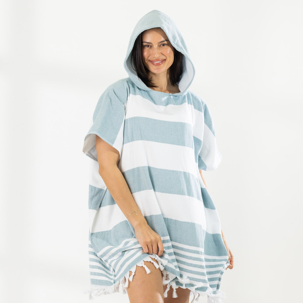 A woman wearing a classic stripe hooded beach poncho with fringed tassels along the hem, photographed against a clean white studio background.