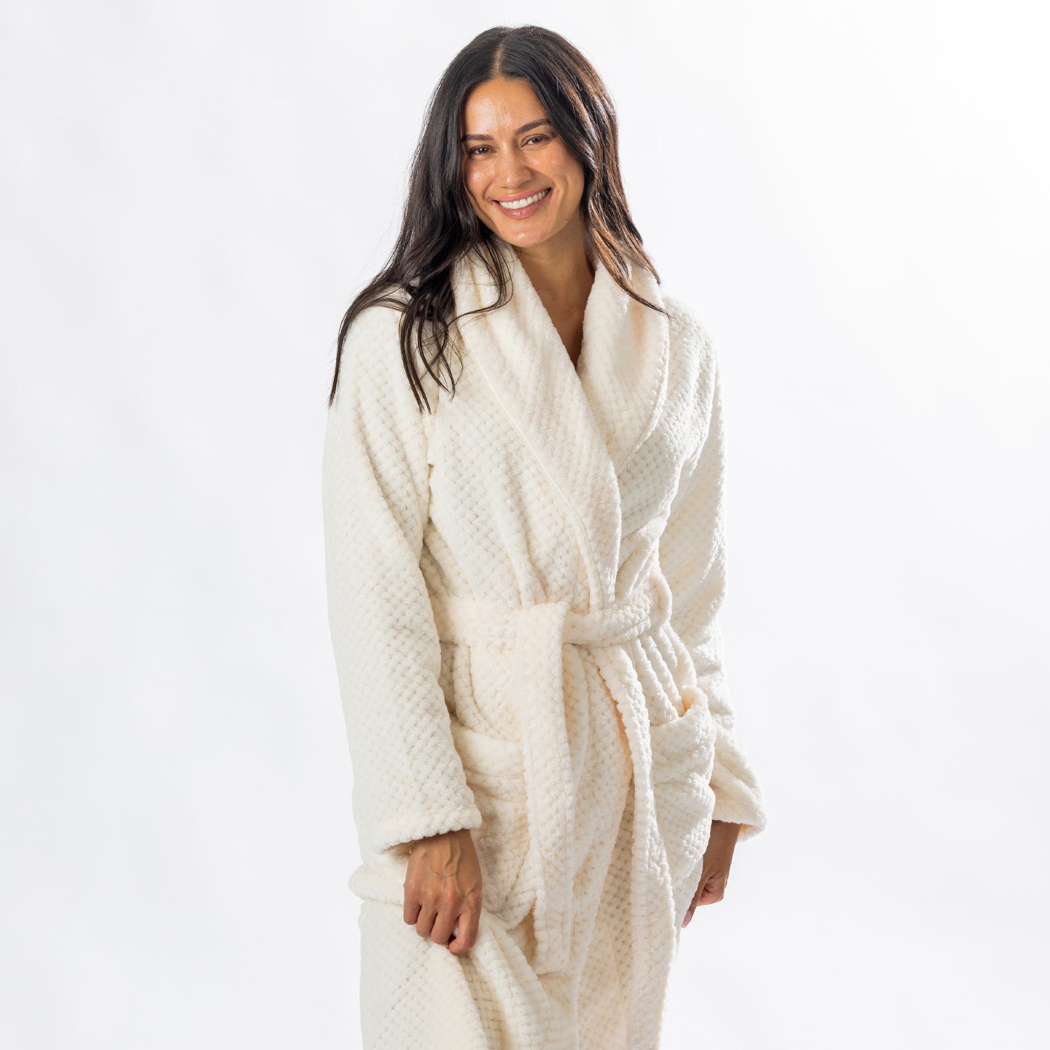 Woman wearing a cream textured plush bathrobe with a shawl collar, self-tie belt and patch pockets.