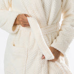 Close-up of the cream textured plush bathrobe showing the soft fabric, shawl collar, self-tie belt and spacious front pocket.