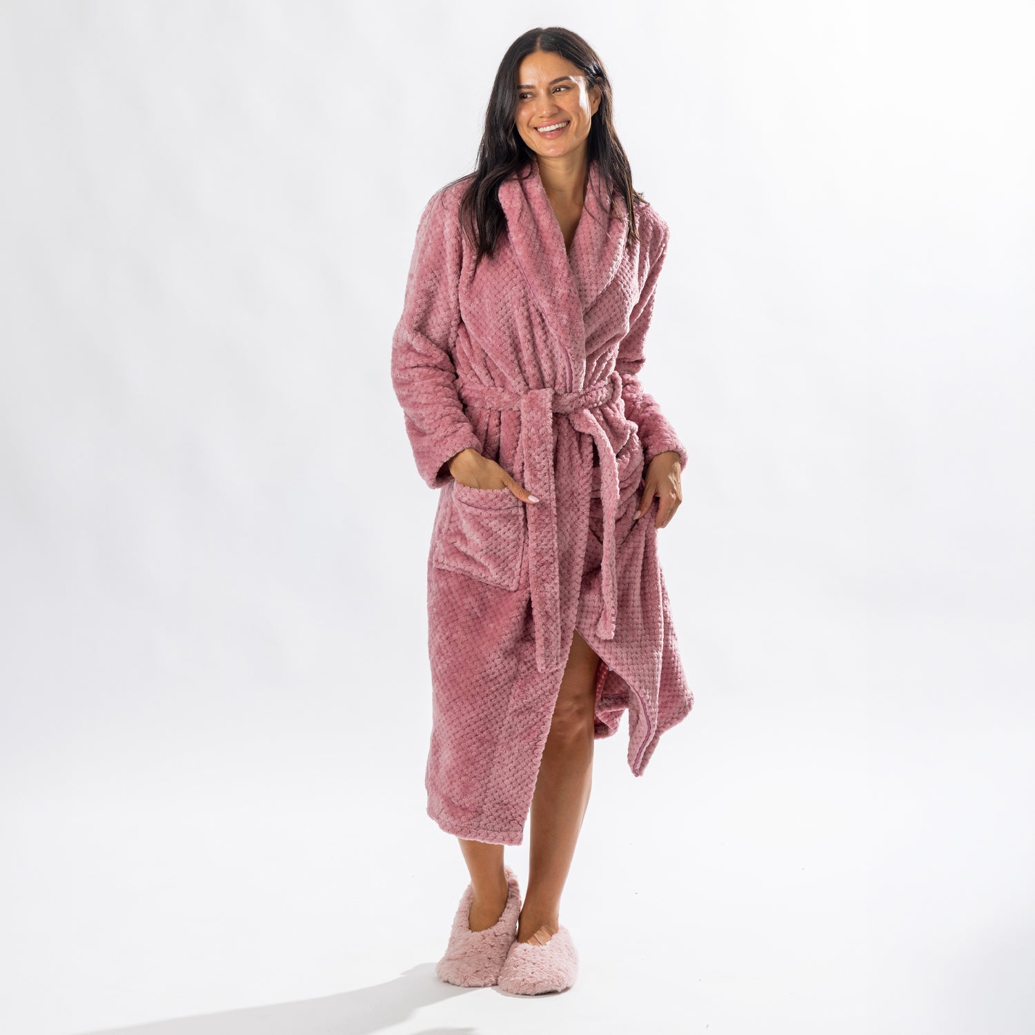 Woman wearing a Rose textured plush bathrobe with a shawl collar, self-tie belt, patch pockets and matching cream slippers.