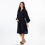 A woman modeling a dark robe with a tie belt and wide sleeves, standing against a plain white studio background.