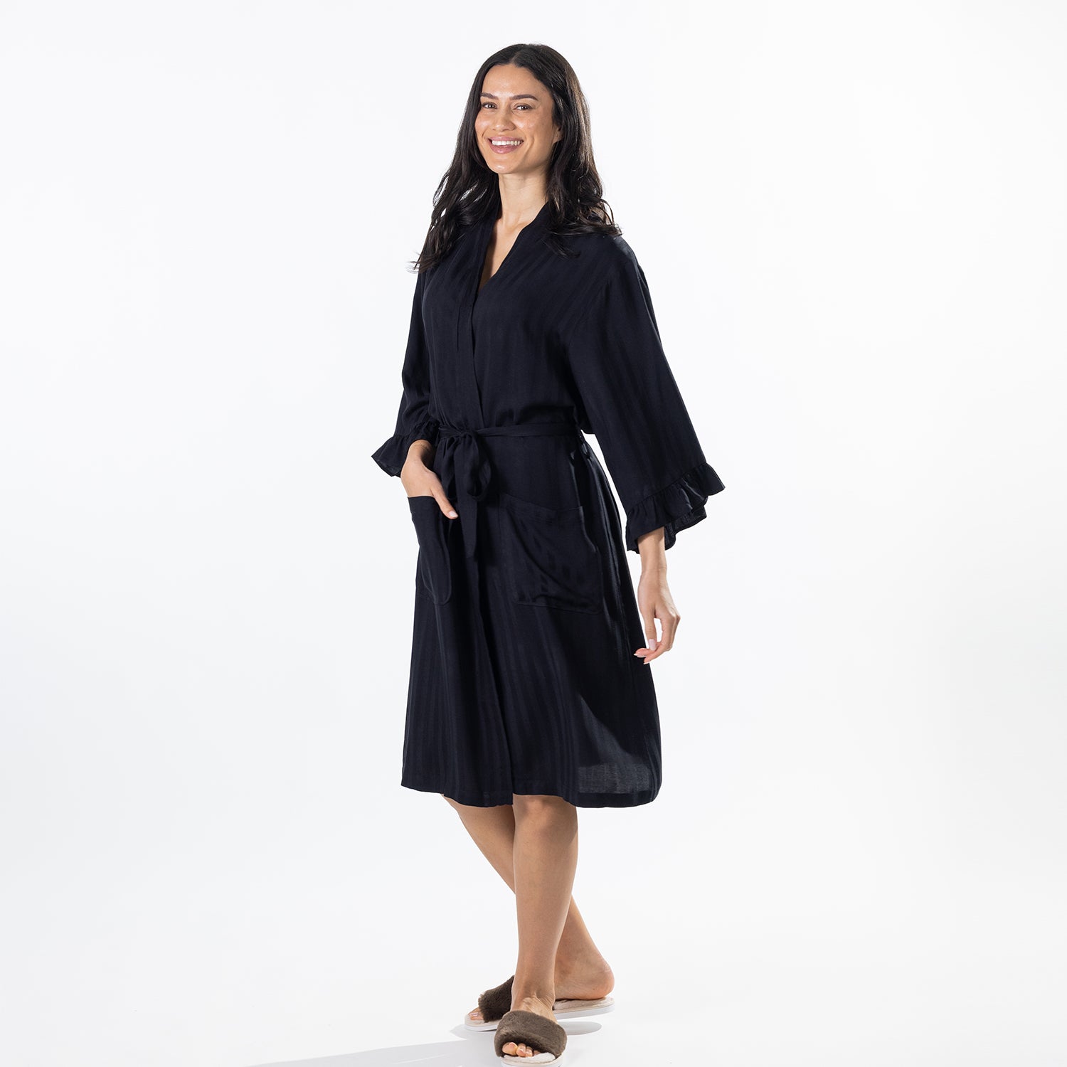 A woman modeling a dark robe with a tie belt and wide sleeves, standing against a plain white studio background.