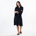 A woman modeling a wrap robe with ruffled sleeves and a tie belt, paired with brown slippers, against a plain white studio background.