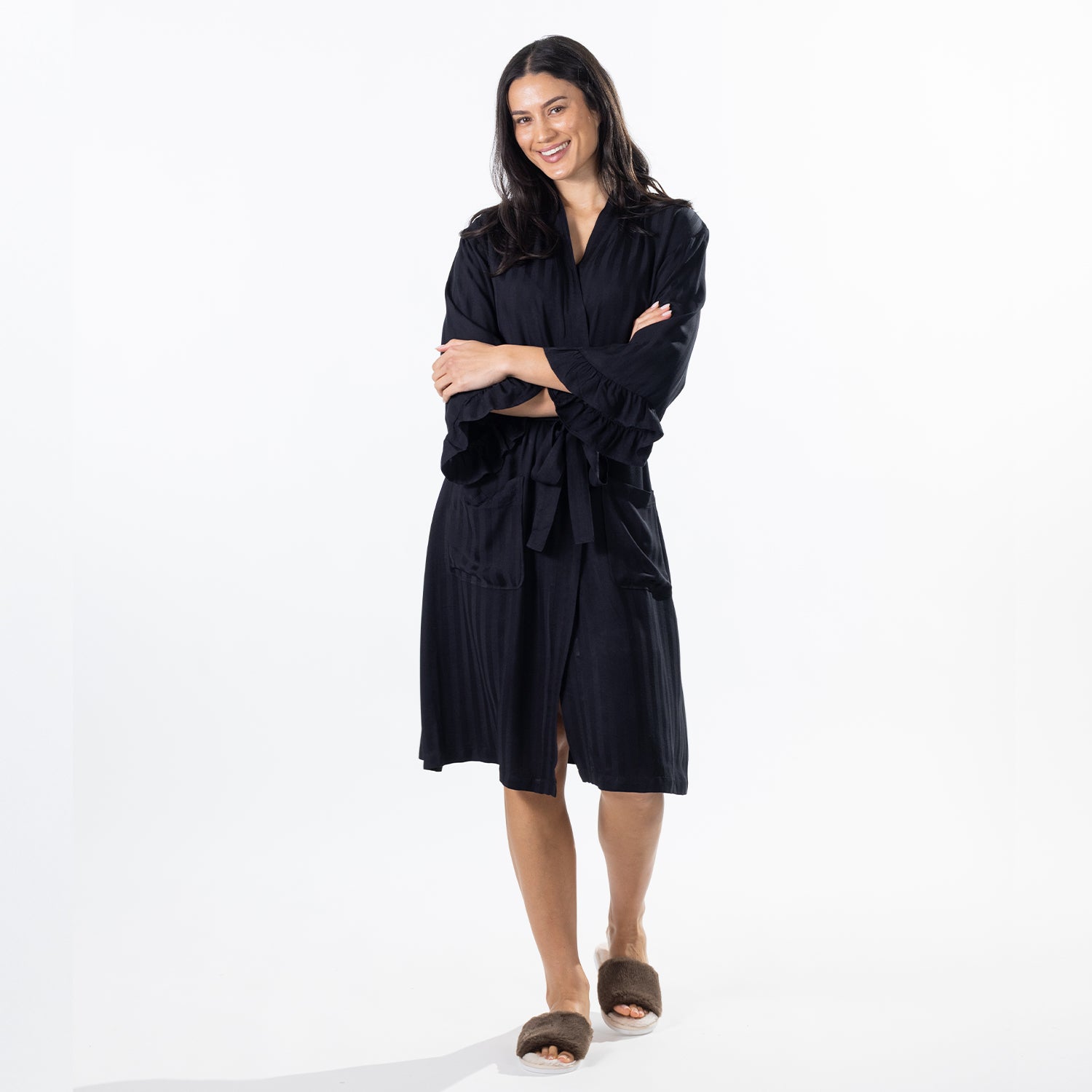 A woman modeling a wrap robe with ruffled sleeves and a tie belt, paired with brown slippers, against a plain white studio background.