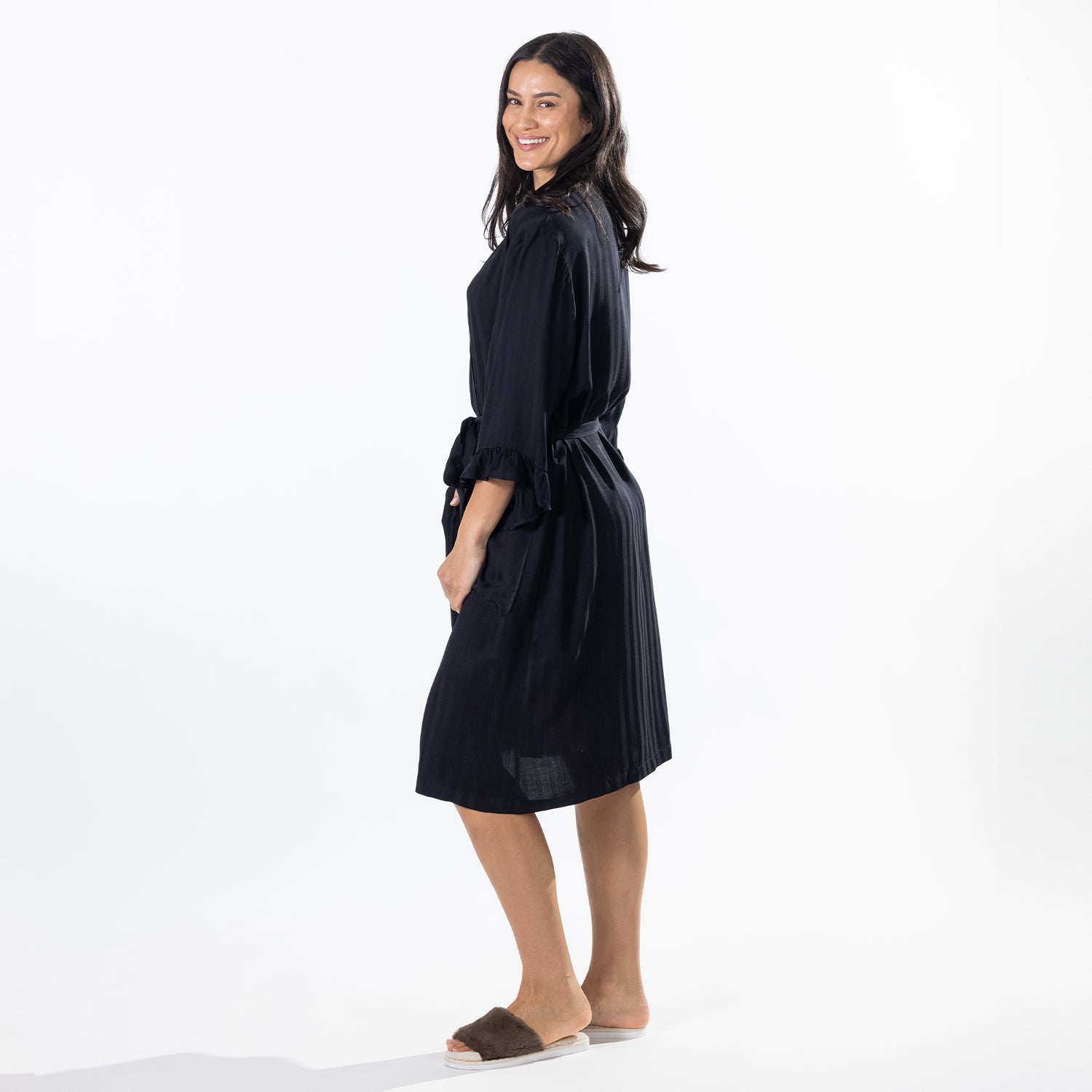 A woman modeling a robe with lace shoulder details, a tie waist belt, and side pockets, paired with brown slide sandals against a white studio background.