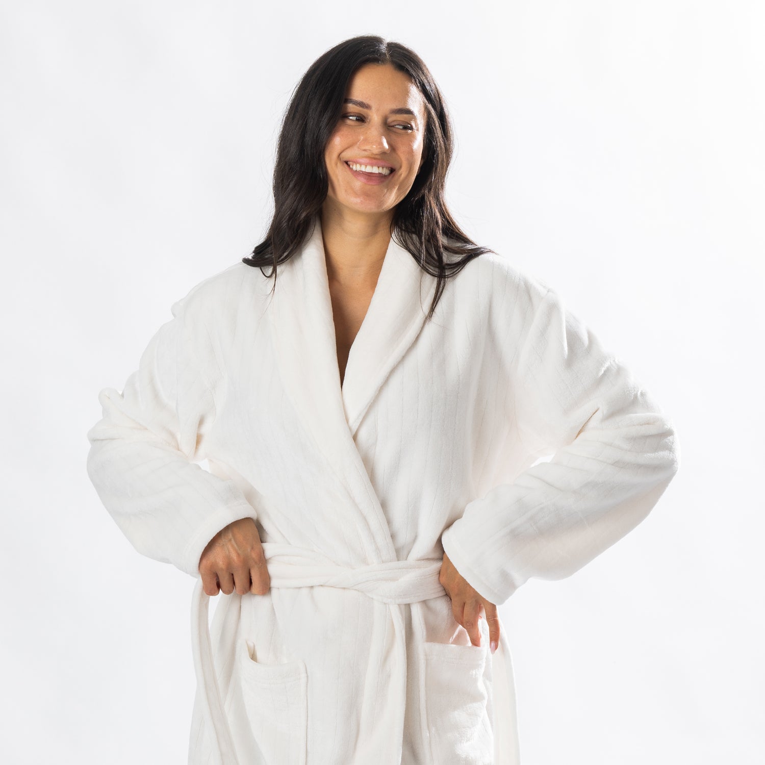 A person wearing a soft, plush cream bathrobe with a waist tie is standing and smiling against a plain light background.