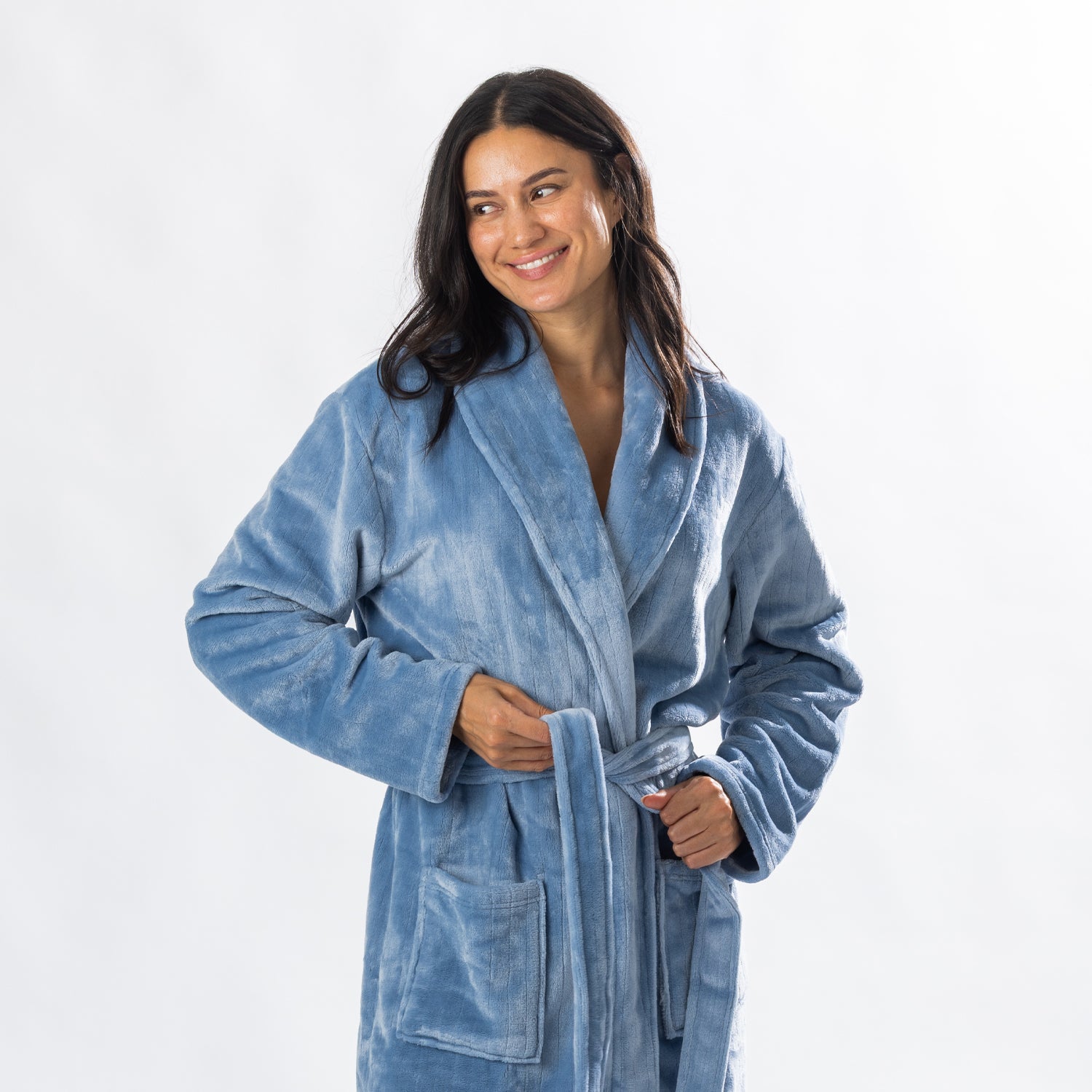 A person wearing a soft, plush pale blue bathrobe with a waist tie is standing and smiling against a plain light background.