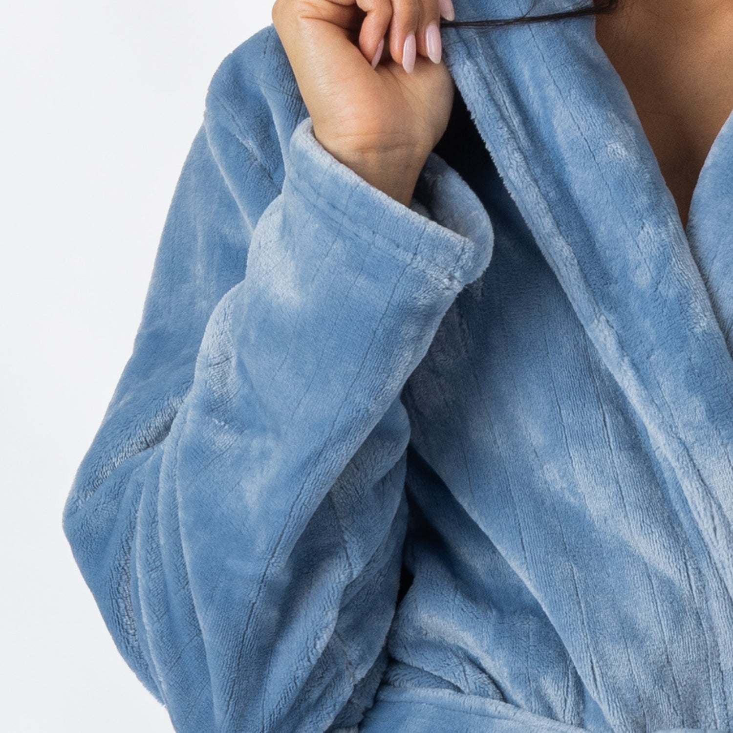 A close-up view of a person wearing a plush pale-blue bathrobe highlights the robe’s soft texture, shawl collar, and sleeve.
