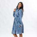 A person wearing a soft, plush pale blue bathrobe with a waist tie is standing and smiling against a plain light background.
