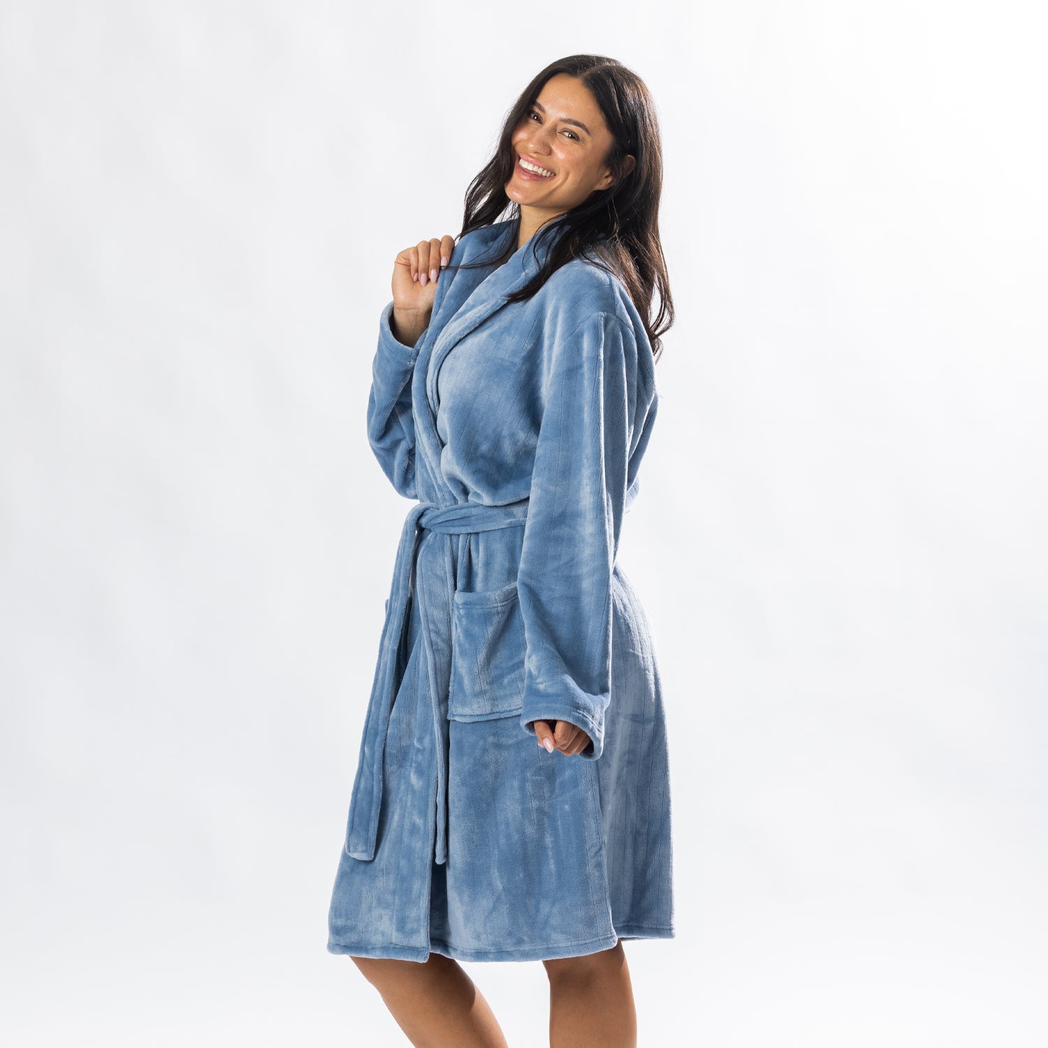 A person wearing a soft, plush pale blue bathrobe with a waist tie is standing and smiling against a plain light background.