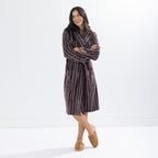 Woman wearing a chocolate brown striped towelling robe with arms folded, highlighting the relaxed fit and front patch pockets.
