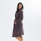 Side profile of a woman wearing a chocolate brown striped towelling robe with hands in pockets, highlighting the robe's silhouette and knee-length design.