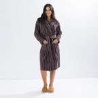 Woman wearing a chocolate brown striped towelling robe with a tie waist and patch pockets, standing front-facing with hands in pockets.