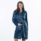 A woman wearing a plush teal waffle bathrobe with a shawl collar and tie belt, standing against a plain white studio background.